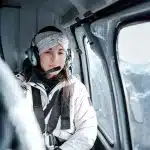 Frau sitzt in einem Helikopter und hat Kopfhörer mit einem mikro auf