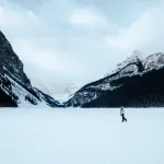 Frau läuft auf dem vereisten und zugeschneiten Lake Louise mit einer Bergkulisse im Hintergrund
