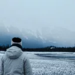 Frau steht mit dem Rücken zur Kamera und schaut auf eine vernebelte Bergkulisse am La Bicher River im Jasper Nationalpark