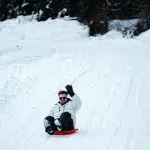 Mann rodelt einen verschneiten Berg hinunter und winkt