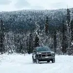 Auto auf zugeschneiter Straße umgeben von Bäumen