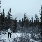 Frau in weißer Jacke läuft durch einen Wald im Winter
