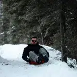 Mann rodelt im Schlitten-Bob einen verschneiten Weg herunter