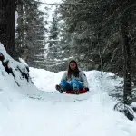 Frau rodelt im Schlitten-Bob einen verschneiten Weg herunter