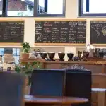 Innenansicht des Murnauer Kaffeehauses mit Tafeln, auf denen Kaffeespezialitäten und Kaffeeregionen dargestellt sind.