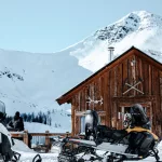 Rustikale Berghütte mit Schneemobilen davor in den Rocky Mountains. Auf der Tour gibt es hier eine Pause mit frisch gegrillten Burgern und einer spektakulären Aussicht.