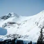 Verschneite Berglandschaft in den kanadischen Rocky Mountains mit blauem Himmel. Die Schneemobil-Tour führt über diesen Pass mit einer Mischung aus schnellen Geraden, engen Kurven und dichten Wäldern.