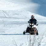 Person sitzt auf einem Schneemobil und fährt auf einer verschneiten Piste