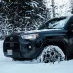 Nahaufnahme eines Toyota 4Runner als Mietwagen in Kanada, der tief im Schnee steht. Die winterliche Kulisse und die schneebedeckten Reifen zeigen die Bedeutung von wintertauglichen Fahrzeugen für Reisen in abgelegene Gebiete.