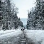 Ein Mietwagen in Kanada fährt auf einer schneebedeckten Waldstraße in den Rocky Mountains. Die verschneite Umgebung und die winterliche Atmosphäre zeigen die Herausforderungen und die Schönheit des Fahrens durch abgelegene Gebiete in Kanada.