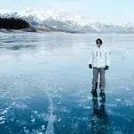 Mann in weißer Winterjacke steht auf dem gefrorenen Abraham Lake mit seinen Methanblasen