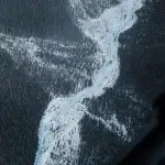 Blick auf einen verschneiten blauen Fluss, der sich durch ein Waldtal windet