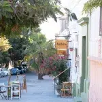 Blick auf die Straße vor dem Café Katkaw in La Paz – mit Straßenschild, bunter Fassade und kleinen Sitzgelegenheiten unter Palmen.