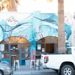 Außenansicht des Poke-Restaurants Blu Fin in La Paz mit farbenfrohem Wandgemälde und Gästen vor dem Eingang.