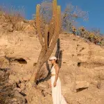 Frau in heller Kleidung steht neben einem hohen Kaktus in der kargen Wüstenlandschaft bei La Paz – goldene Abendsonne trifft auf Baja-Feeling.