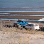 Pick-up-Trucks und Pavillon am Rand der Dünen von El Mogote – typischer Wochenendspot der Locals direkt am Wasser.