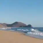 Eine unberührte, weite Sandküste bei Todos Santos mit ruhigen Wellen und felsigen Hügeln im Hintergrund – ein idealer Ort für lange Spaziergänge und Naturerlebnisse.