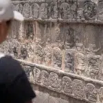 Person steht vor einer Steinmauer, in die Köpfe eingemeißelt sind