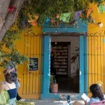 Blauer Eingang zum Café Once in Oaxaca mit einer gelber Fassade, davor auf der Terrasse sitzen Menschen