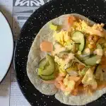 Tacos mit GUrken, Gemüse und Fisch auf einem schwarzen Teller