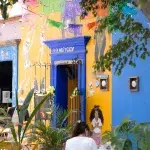 Bunte Fassade des Restaurants De Maiz y Cacao, wo draußen auf der Terrasse eine Frau sitzt