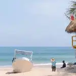 Blick auf das Meer und den Strand auf dem ein Boot steht und rechts der Turm der Lifeguards steht