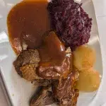 Teller mit saftigem Braten, Rotkohl und einer üppigen Portion Bratensoße.