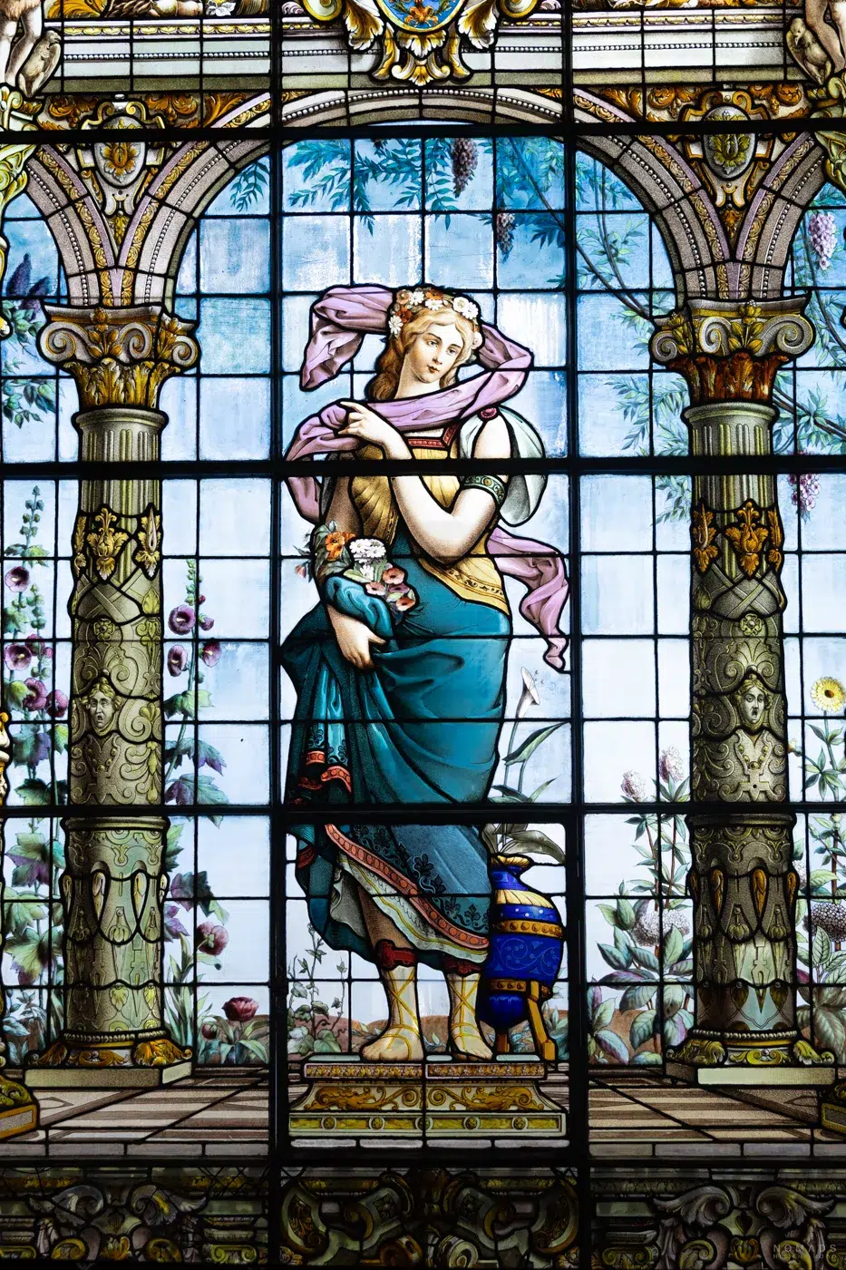 Detailreiche Glasmalerei im Castillo de Chapultepec, die eine historische Frauenfigur mit Blumen und klassischen Säulen zeigt.