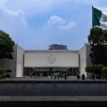Monumentales Eingangsportal des Museo Nacional de Antropología in Mexiko-Stadt mit großer mexikanischer Flagge.