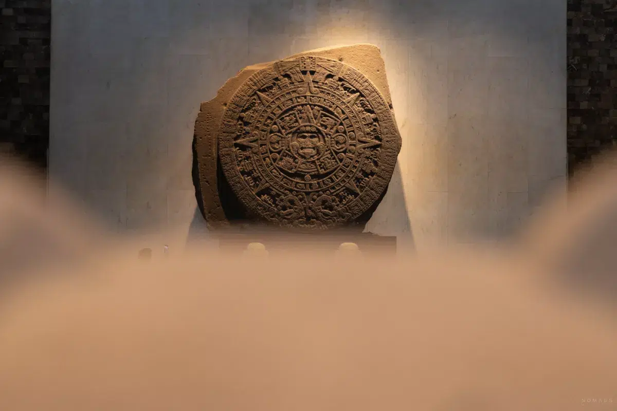 Die berühmte Azteken-Sonnenscheibe im Museo Nacional de Antropología in Mexiko-Stadt, beleuchtet an einer Wand aus hellem Stein.