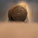 Die berühmte Azteken-Sonnenscheibe im Museo Nacional de Antropología in Mexiko-Stadt, beleuchtet an einer Wand aus hellem Stein.
