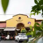 Außenansicht des Mercado de Coyoacán mit gelber Fassade, Arkaden und parkenden Autos im Vordergrund