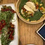 Moderne mexikanisch-asiatische Küche mit gefüllten Bao Buns und Tacos auf einem Holztisch in Mexiko City