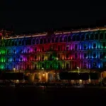 Historisches Regierungsgebäude am Zócalo in Mexiko-Stadt bei Nacht, beleuchtet in Regenbogenfarben während des Pride Month
