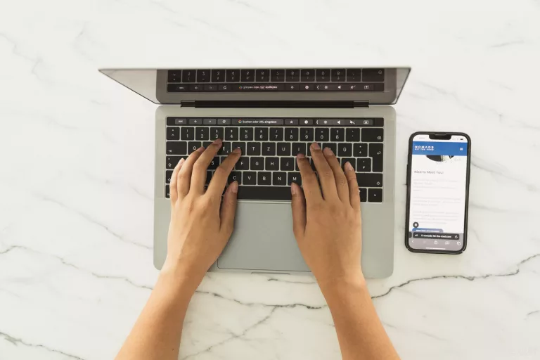 Person tippt auf einem MacBook, daneben liegt ein iPhone mit geöffneter Website von Nomads Hit The Road – Symbolbild für mobiles Arbeiten und sicheres Surfen unterwegs.