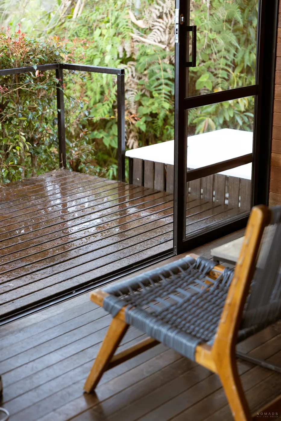 Holzterrasse und moderner Stuhl im Boato Hotel in Guatapé, Kolumbien, mit Blick ins Grüne nach einem Regenschauer.