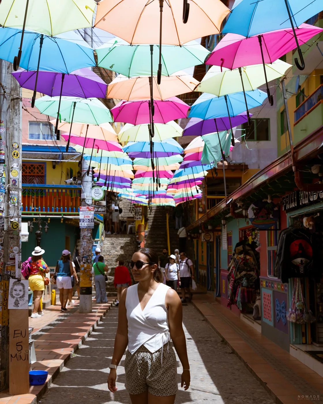 Touristin geht durch farbenfrohe Gasse in Guatapé, Kolumbien, unter einer Installation aus bunten Regenschirmen