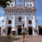 Frontansicht der Iglesia Nuestra Señora del Carmen in Guatapé, Kolumbien, mit rotem und weißem Kolonialstil und Besuchern vor dem Eingang.