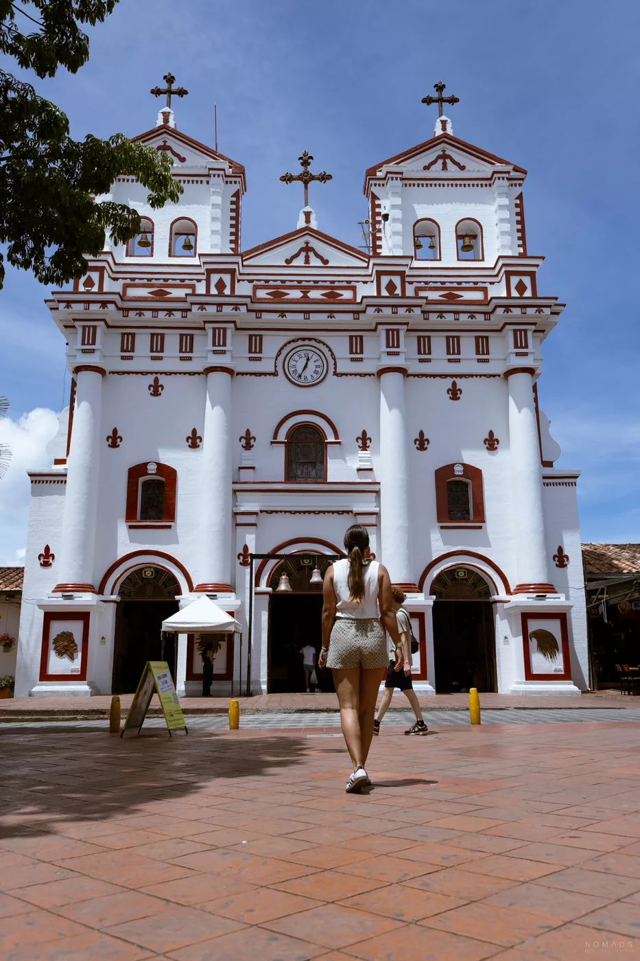 Frontansicht der Iglesia Nuestra Señora del Carmen in Guatapé, Kolumbien, mit rotem und weißem Kolonialstil und Besuchern vor dem Eingang.