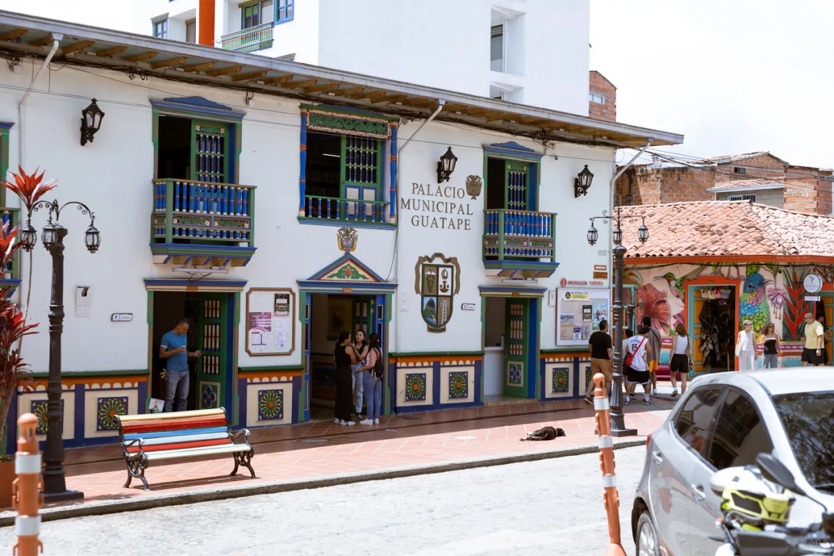 Fassade des Palacio Municipal in Guatapé, Kolumbien, mit bunten Holzverzierungen und Menschen vor dem Eingang.