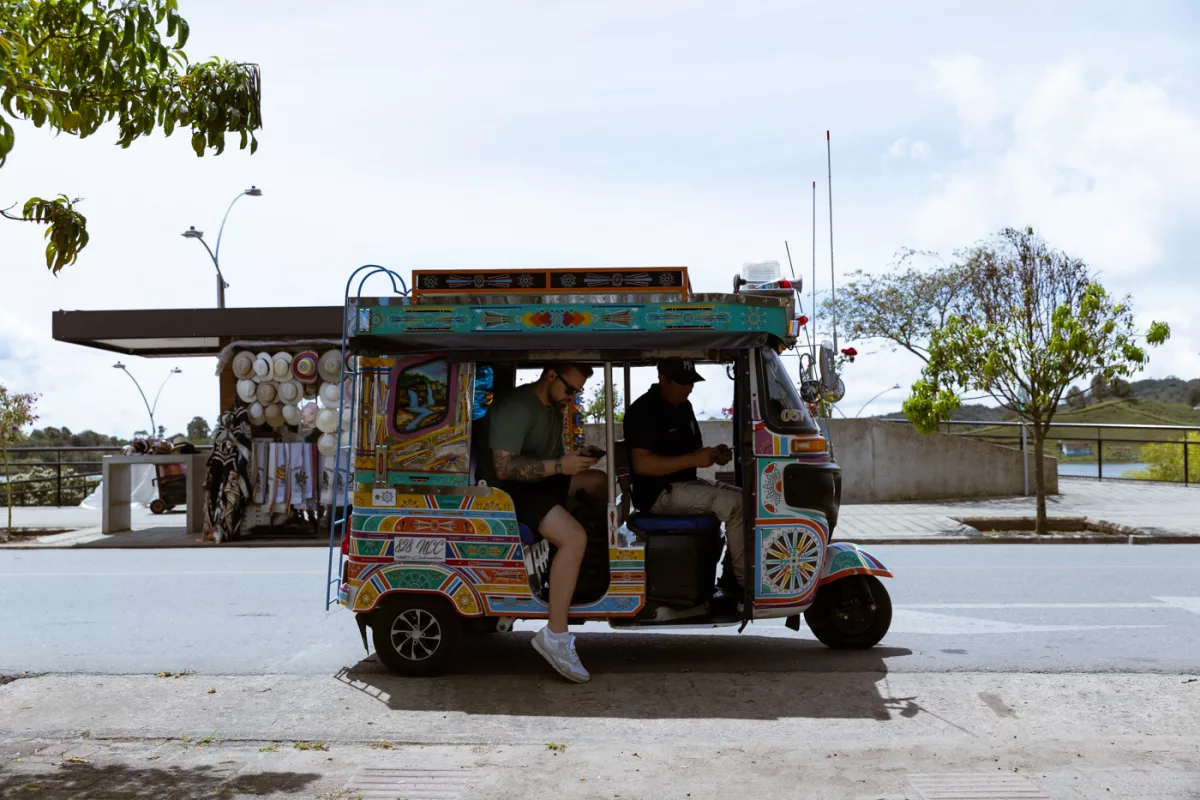 Farbenfrohes TukTuk in Guatapé, Kolumbien, mit zwei Fahrgästen, geparkt an der Straße nahe Souvenirständen