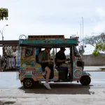 Farbenfrohes TukTuk in Guatapé, Kolumbien, mit zwei Fahrgästen, geparkt an der Straße nahe Souvenirständen