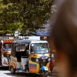 Bunt bemaltes TukTuk in Guatapé, Kolumbien, vor Bäumen und Straßenständen – typisches Transportmittel für Touristen