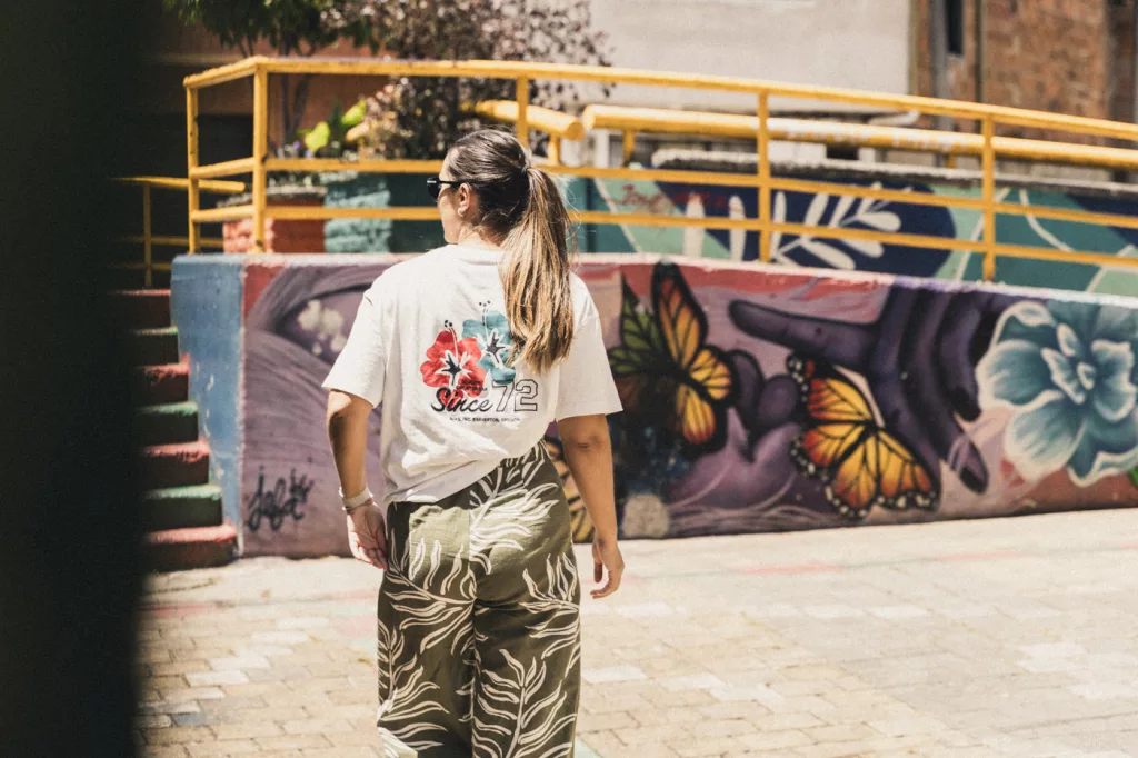 Frau läuft durch die Straßen Medellins. Im Hintergrund sind bunte Wandmalereien zu sehen.