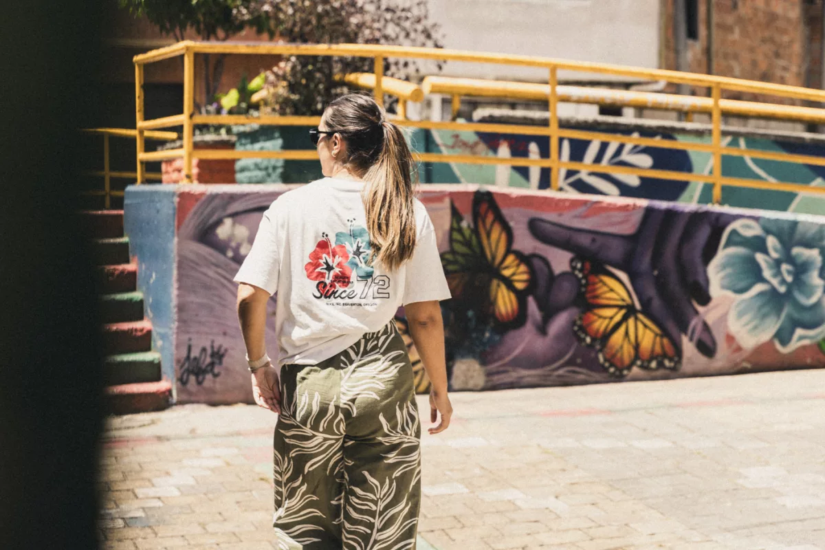 Frau läuft durch die Straßen Medellins. Im Hintergrund sind bunte Wandmalereien zu sehen.