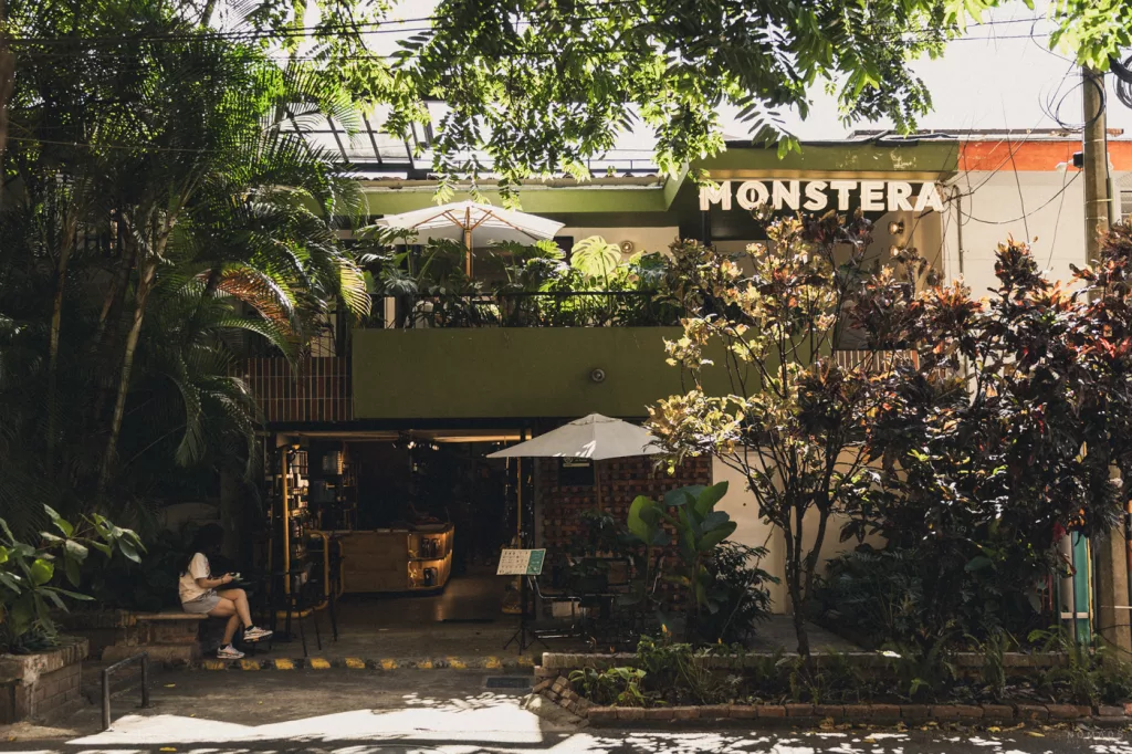 Das Café Monstera in Medellín, Kolumbien – grüne Fassade mit viel Pflanzen, Terrasse mit Sonnenschirmen und gemütlicher Atmosphäre.