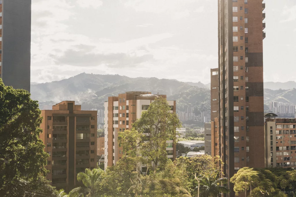 Blick über die Hochhäuser von Medellín mit grünen Bäumen im Vordergrund und den Anden im Hintergrund.