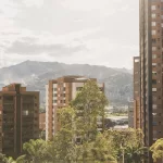 Blick über die Hochhäuser von Medellín mit grünen Bäumen im Vordergrund und den Anden im Hintergrund.