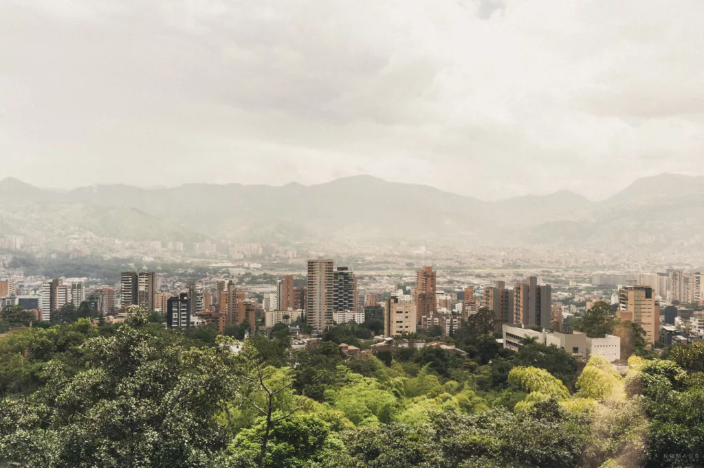 Panoramablick über Medellín mit Hochhäusern, dichtem Grün im Vordergrund und den Bergen des Aburrá-Tals im Hintergrund unter bewölktem Himmel.