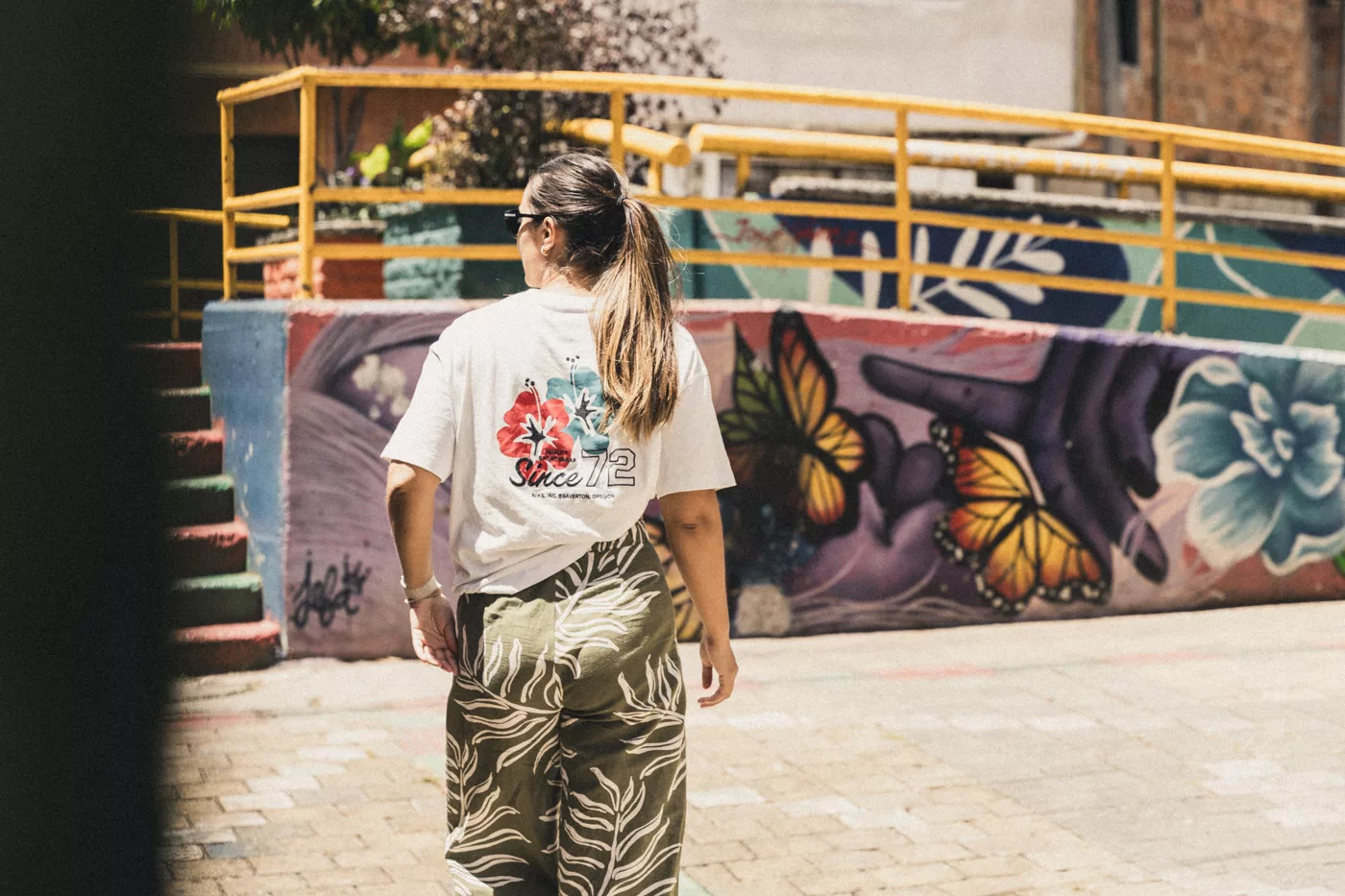 Frau läuft durch die Straßen Medellins. Im Hintergrund sind bunte Wandmalereien zu sehen.